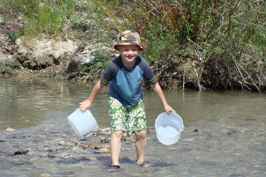A young boy playing with buckets in a creek.