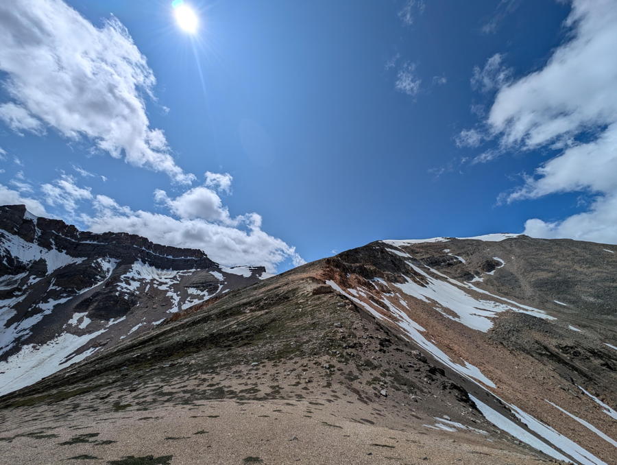An alpine ridge narrows to a distant, snowcapped summit